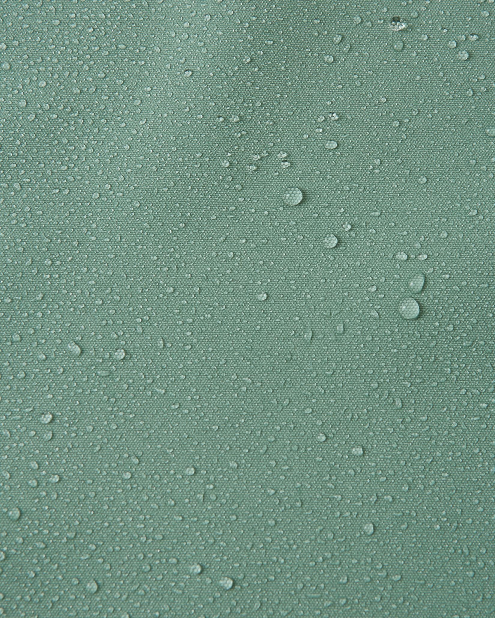 Macro close-up of water droplets beading and rolling off the surface of the Reima Suojala kids' stone green shell jacket, demonstrating its highly waterproof, dirt-repellent Reimatec material.