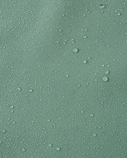 Macro close-up of water droplets beading and rolling off the surface of the Reima Suojala kids' stone green shell jacket, demonstrating its highly waterproof, dirt-repellent Reimatec material.