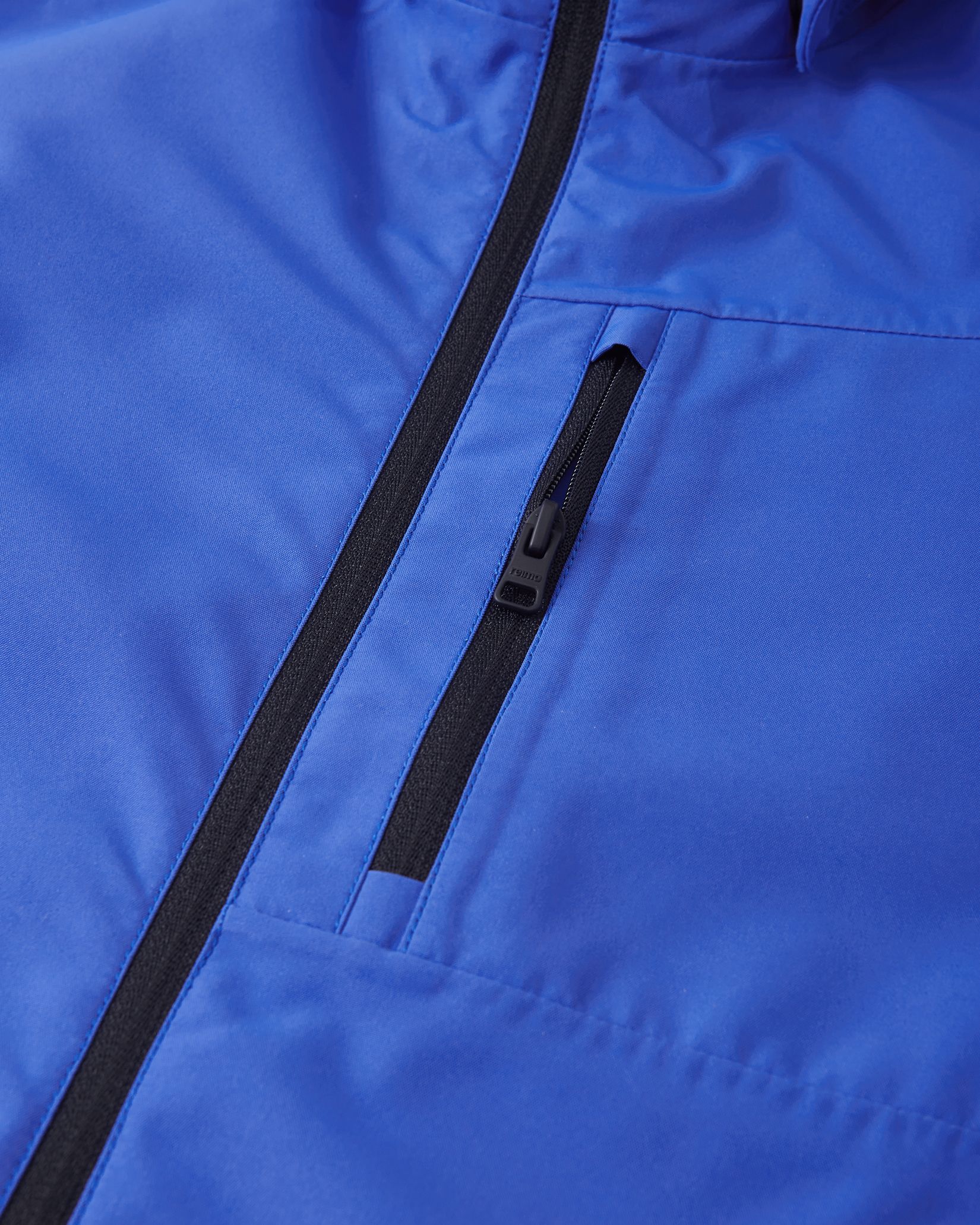 Close-up of the secure, vertical zippered chest pocket on the Reima Suojala kids waterproof jacket in sparkly blue.