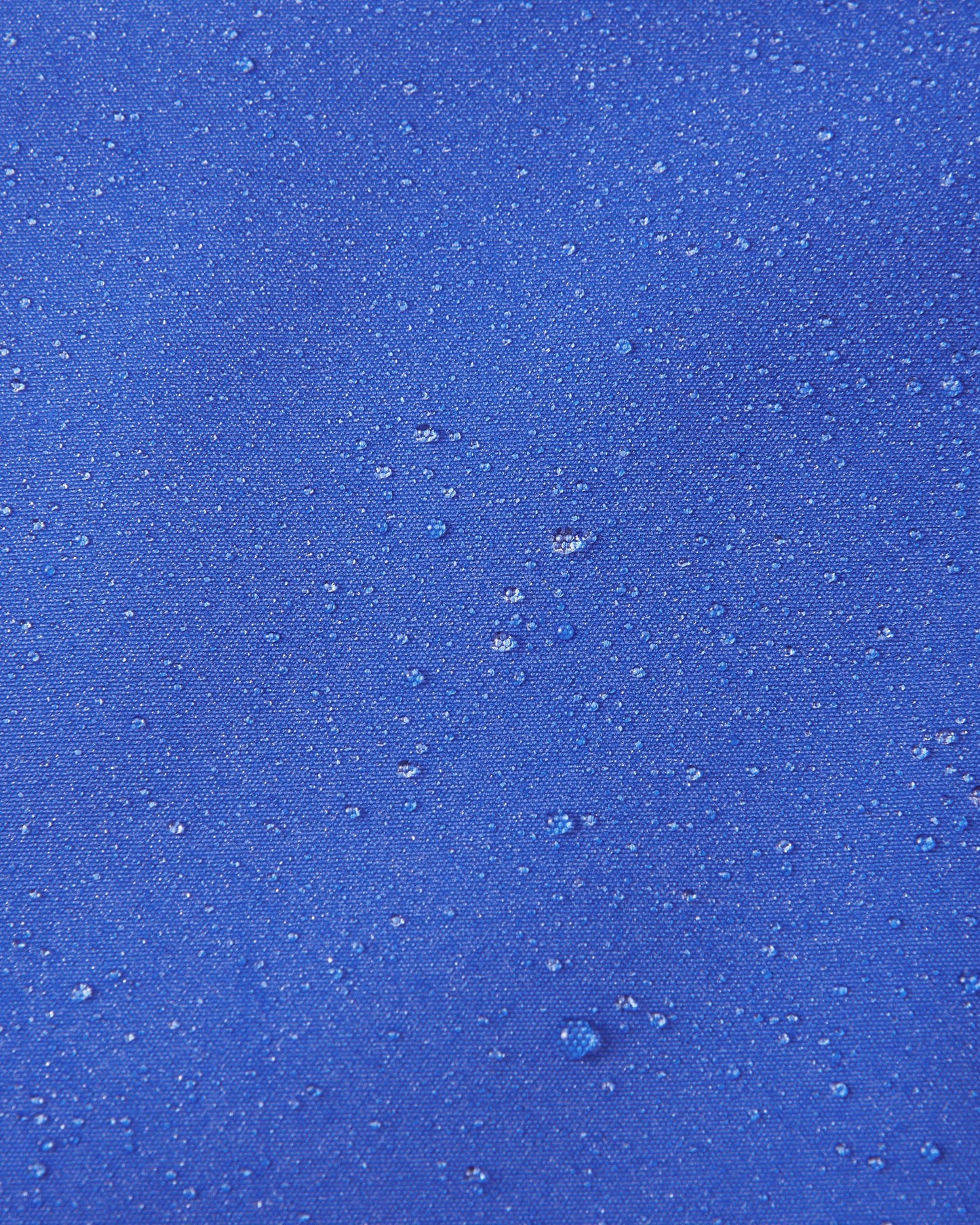 Close-up of water droplets beading on the sparkly blue fabric of the Reima Suojala kids jacket, demonstrating its waterproof capabilities.