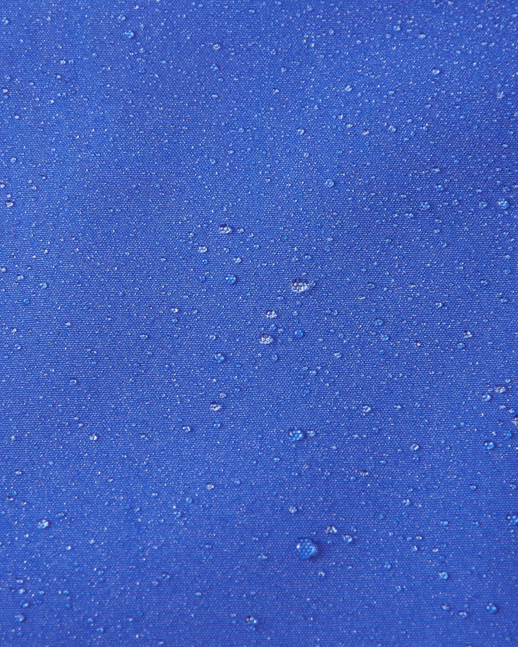 Close-up of water droplets beading on the sparkly blue fabric of the Reima Suojala kids jacket, demonstrating its waterproof capabilities.