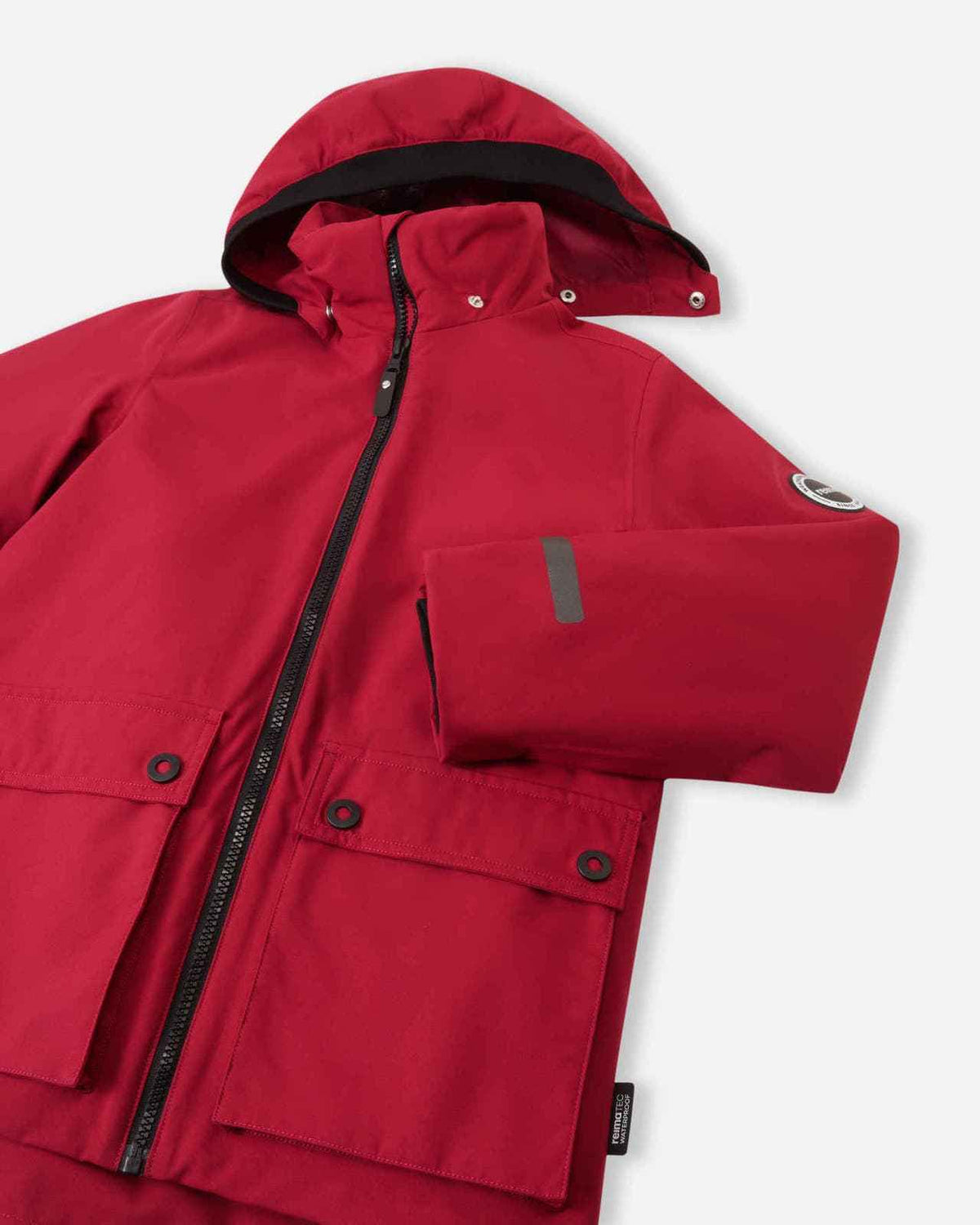 Close-up detail of the front of the Reima Syddi 3-in-1 kids jacket in cranberry red, highlighting the sturdy main zipper, large dual-snap flap pockets, and the smooth dark lining of the hood.