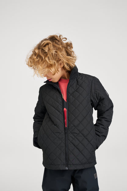 A child modeling the lightweight black quilted inner layer of the Reima Syddi 3-in-1 kids jacket, demonstrating how it can be worn separately as a warm and comfortable standalone jacket.