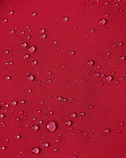 A close-up texture shot demonstrating water droplets cleanly beading up on the cranberry red waterproof exterior fabric of the Reima Syddi 3-in-1 kids jacket.