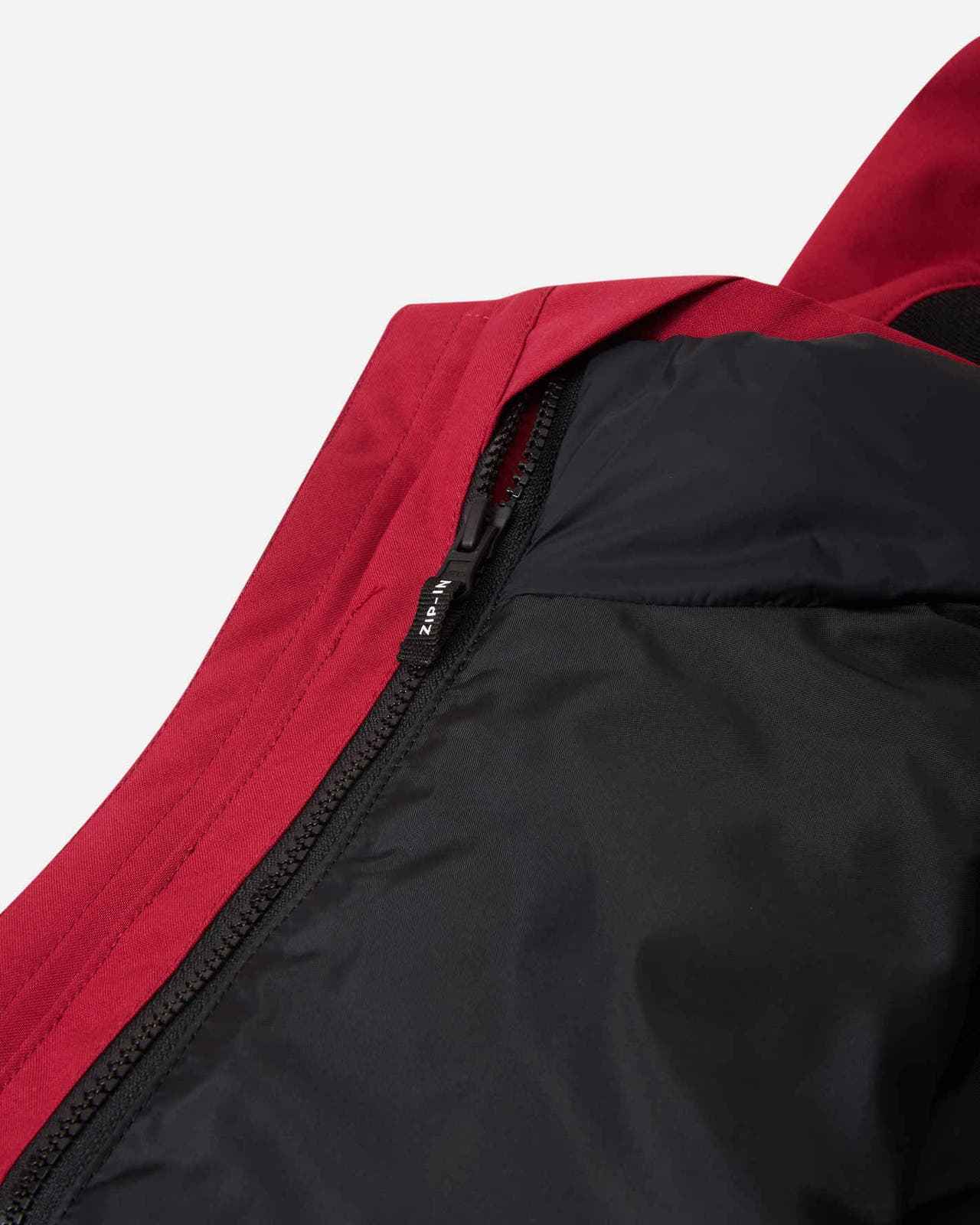Close-up detail of the interior of the Reima Syddi 3-in-1 kids jacket, showing the specialized zip-in system used to securely and easily attach the cranberry red outer shell to the inner quilted layer.