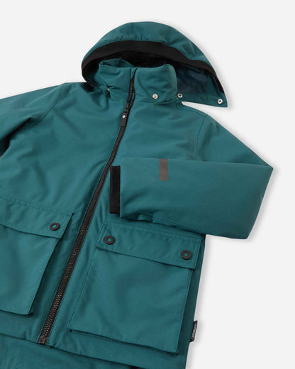 Close-up of the Reima Syddi kids' 3-in-1 jacket in dark teal, highlighting the smooth outer fabric, detachable hood lining, and front flap pockets.