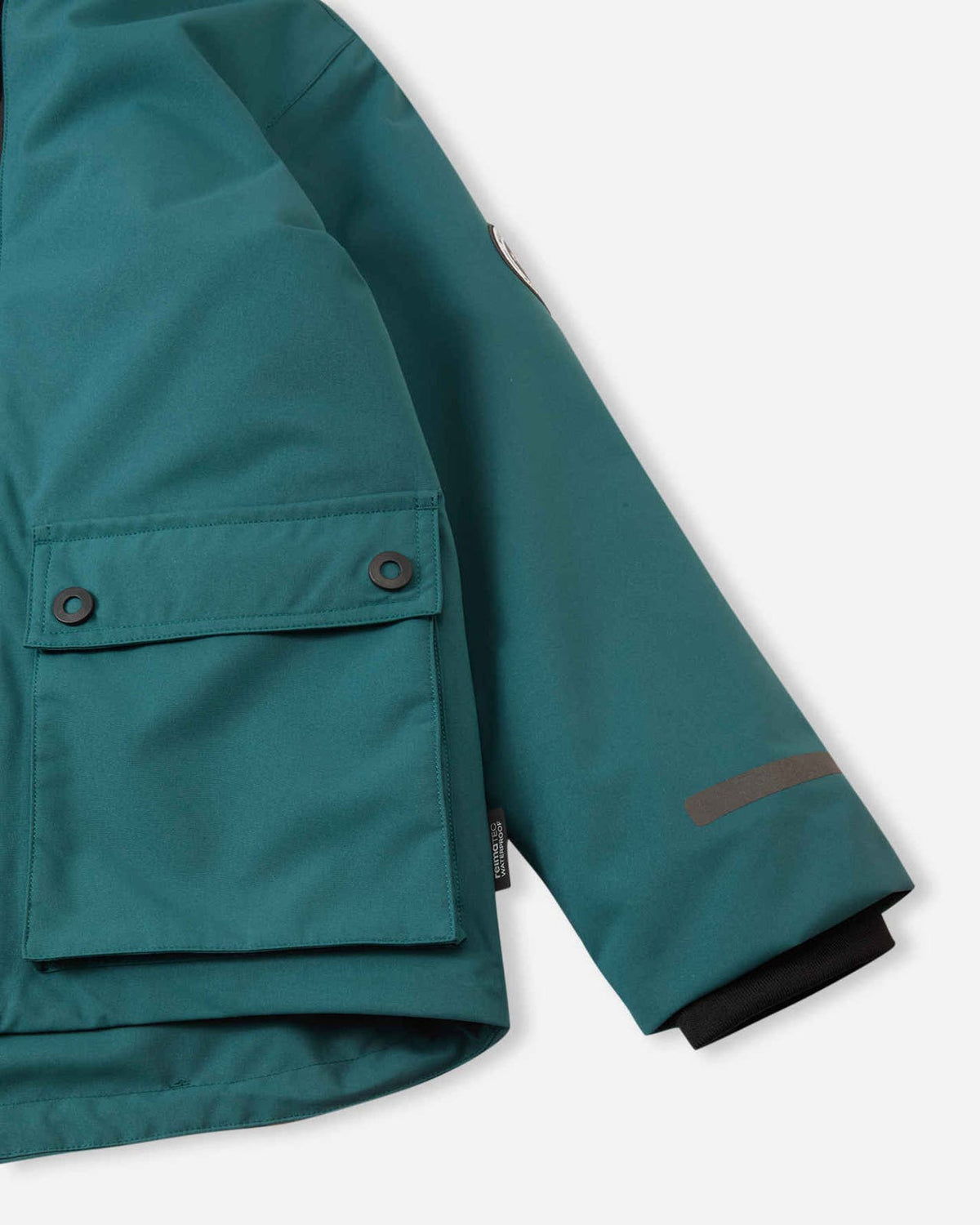 Close-up of the snap-button flap pocket, adjustable sleeve cuff, and reflective sleeve detailing on the dark teal Reima Syddi kids' jacket.