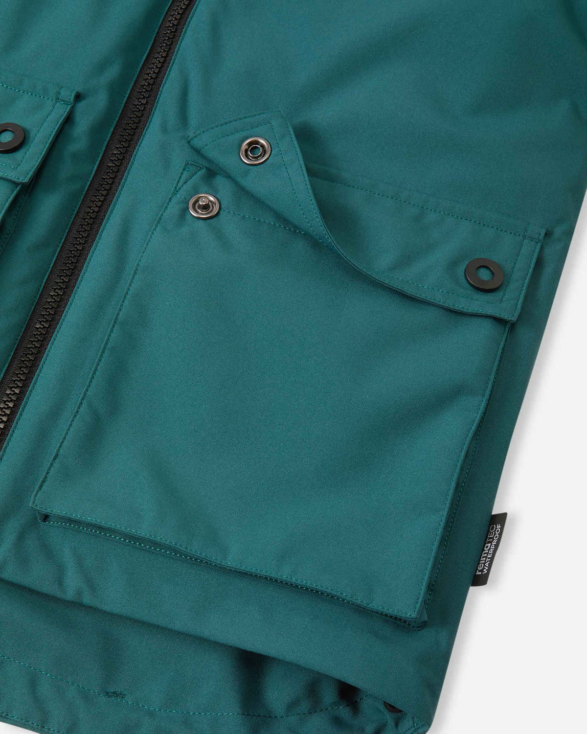 Detail shot of the two large front flap pockets on the Reima Syddi kids' dark teal jacket, showing the durable snap button closures.