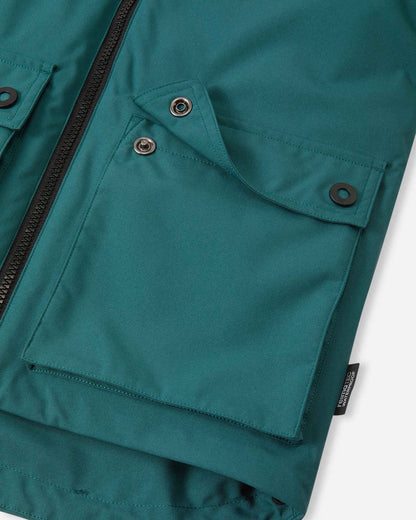 Detail shot of the two large front flap pockets on the Reima Syddi kids' dark teal jacket, showing the durable snap button closures.