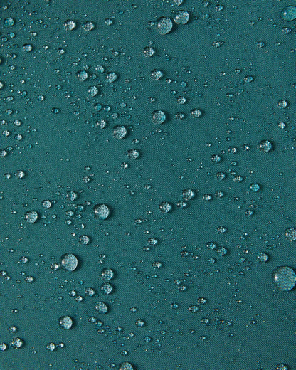 Close-up of water droplets beading on the dark teal Reimatec fabric of the Syddi kids' jacket, demonstrating its waterproof and weather-resistant properties.