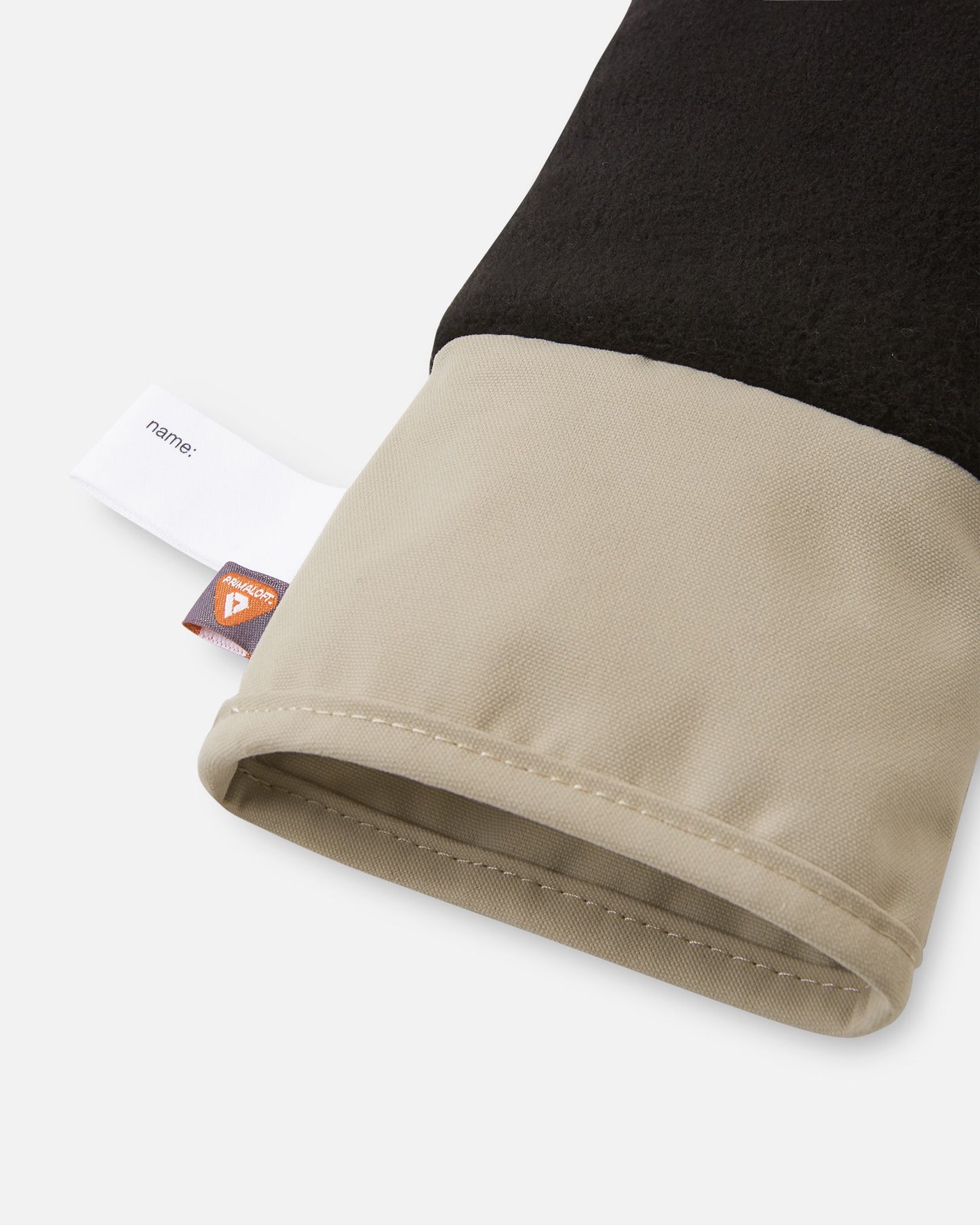 Detail of the inner cuff of the earthy beige Reima Tartu kids' winter gloves, showing the cozy black fleece lining, a built-in name tag, and the eco-friendly PrimaLoft insulation label.