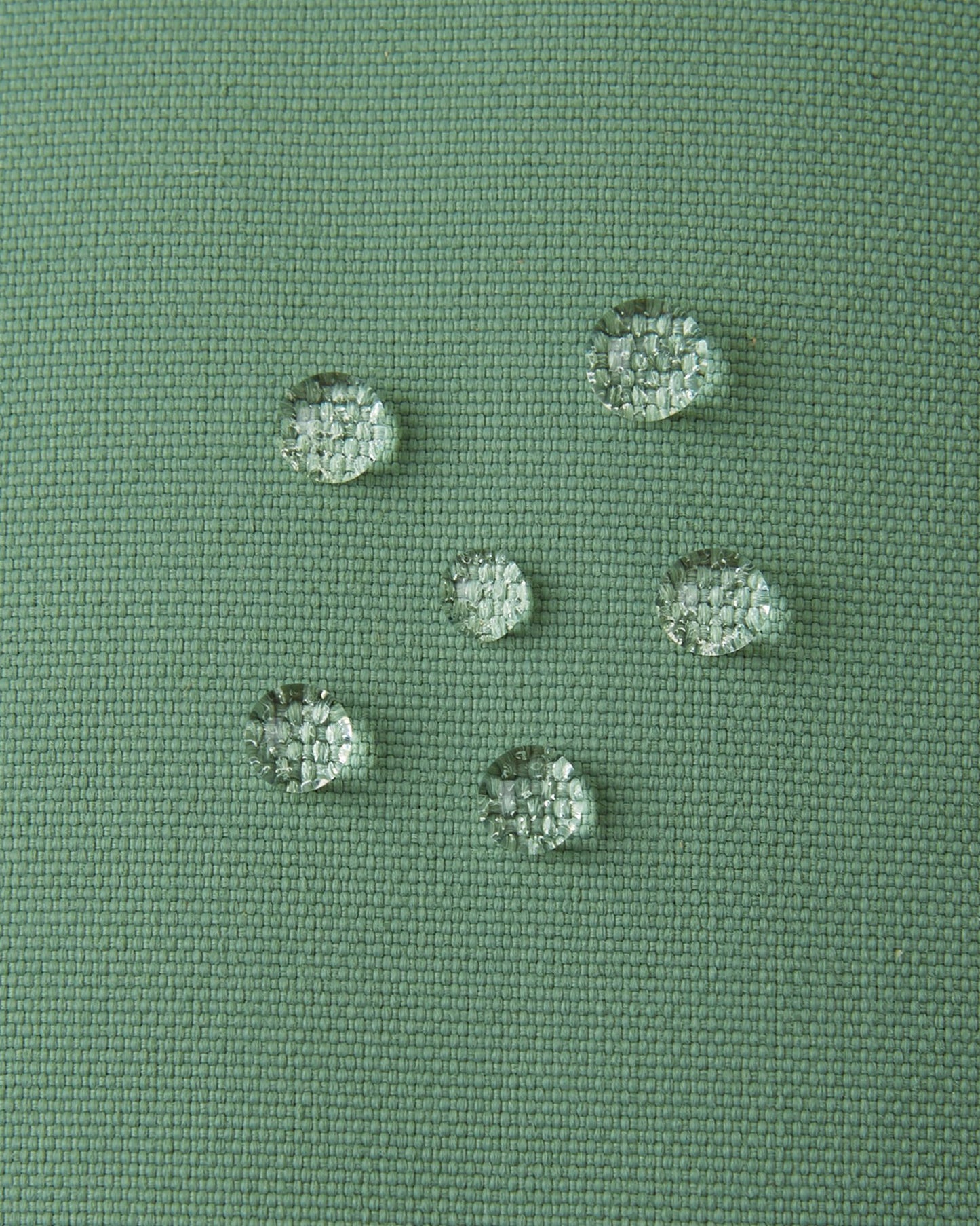 Macro close-up of water droplets actively beading and rolling off the green clay outer shell of the Reima Tartu kids' winter gloves, demonstrating the high-performance waterproof Reimatec technical fabric.