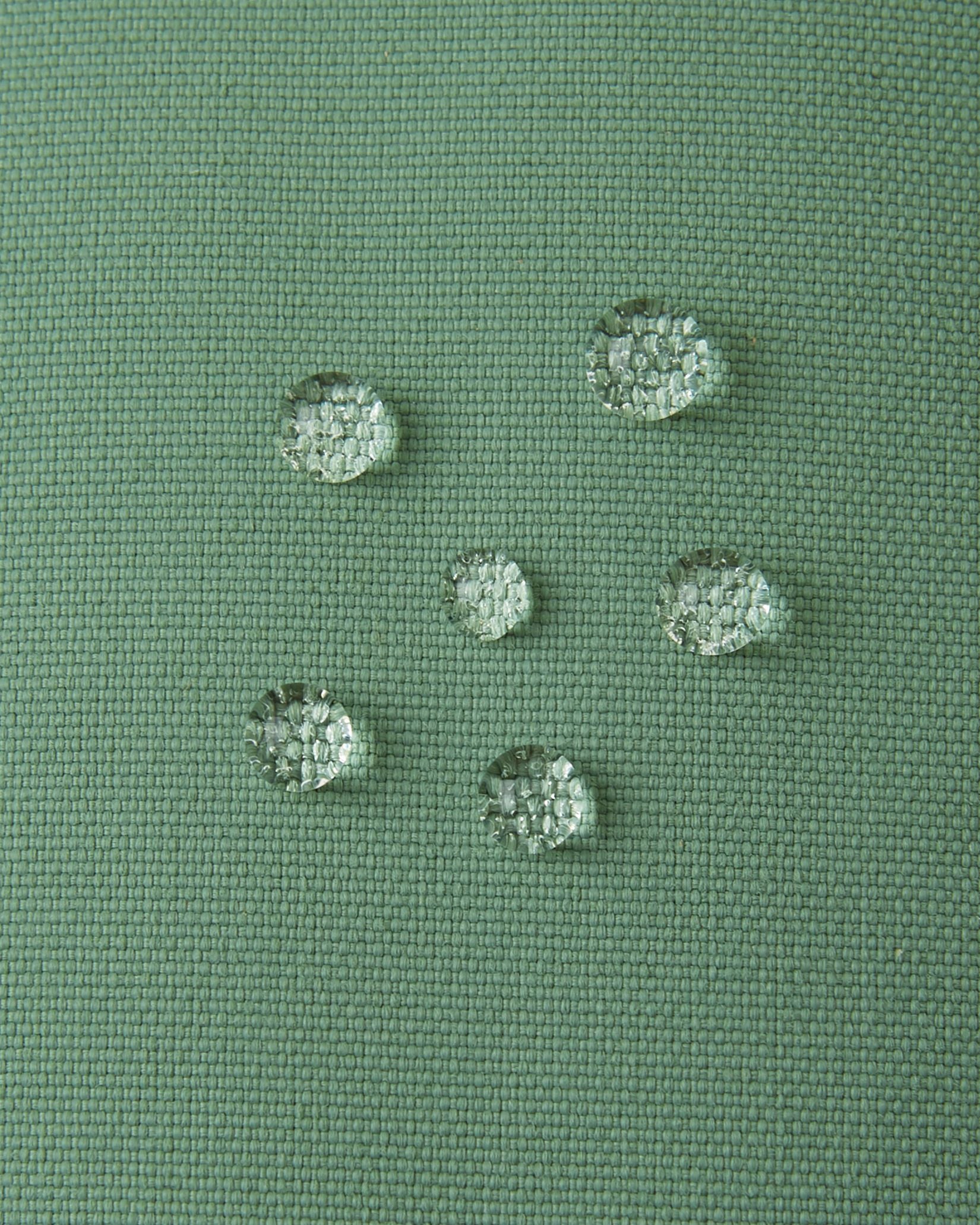 Macro close-up of water droplets actively beading and rolling off the green clay outer shell of the Reima Tartu kids' winter gloves, demonstrating the high-performance waterproof Reimatec technical fabric.