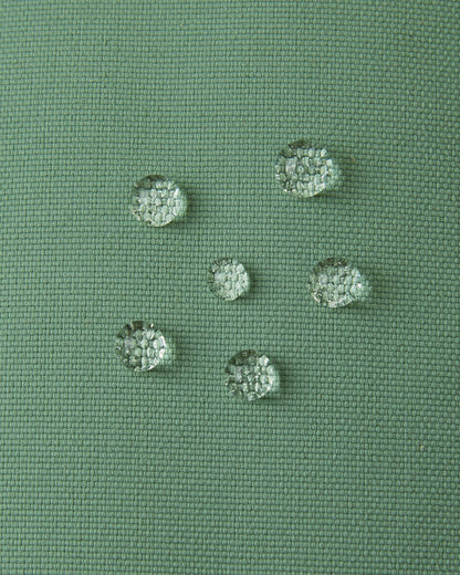 Macro close-up of water droplets actively beading and rolling off the green clay outer shell of the Reima Tartu kids' winter gloves, demonstrating the high-performance waterproof Reimatec technical fabric.