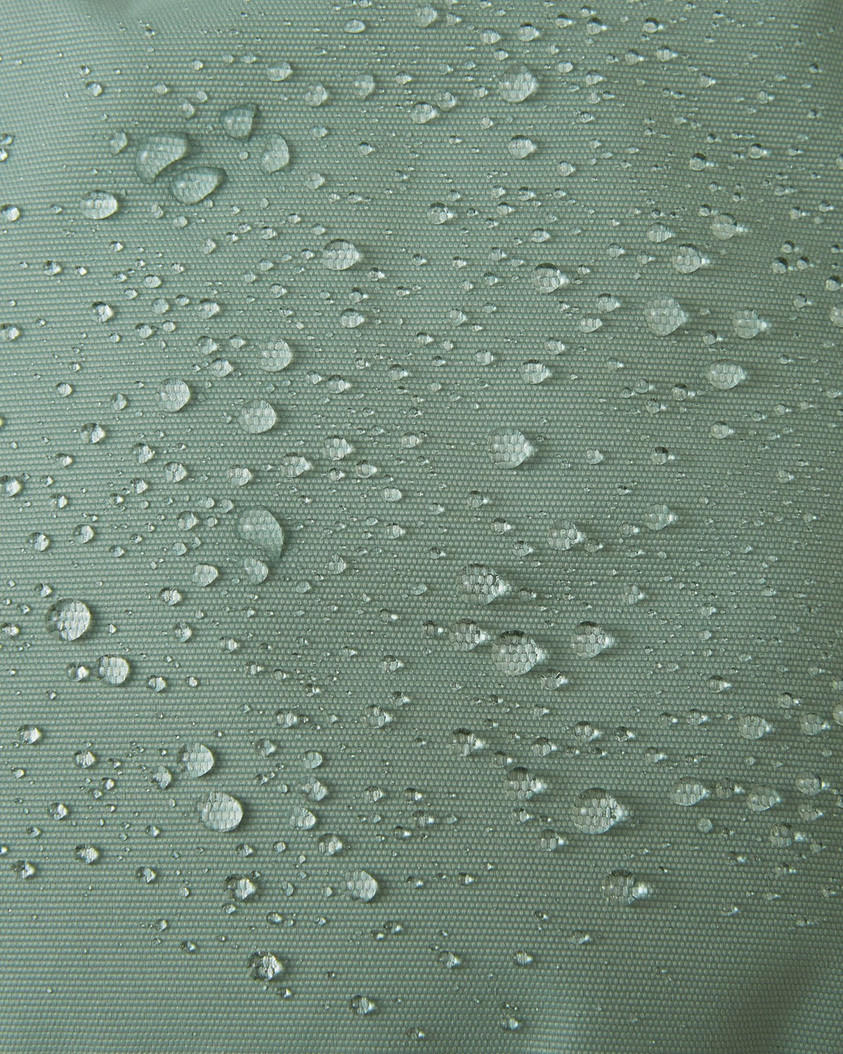 Macro texture shot of the stone green Reima Tassuin toddler mittens, showing water droplets perfectly beading on the woven exterior to demonstrate the fabric's durable water-repellent and weatherproof qualities.