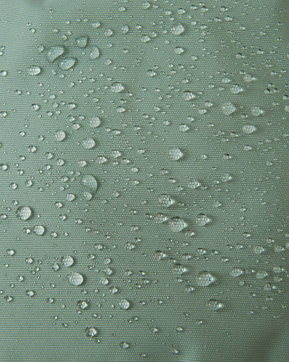 Macro texture shot of the stone green Reima Tassuin toddler mittens, showing water droplets perfectly beading on the woven exterior to demonstrate the fabric's durable water-repellent and weatherproof qualities.