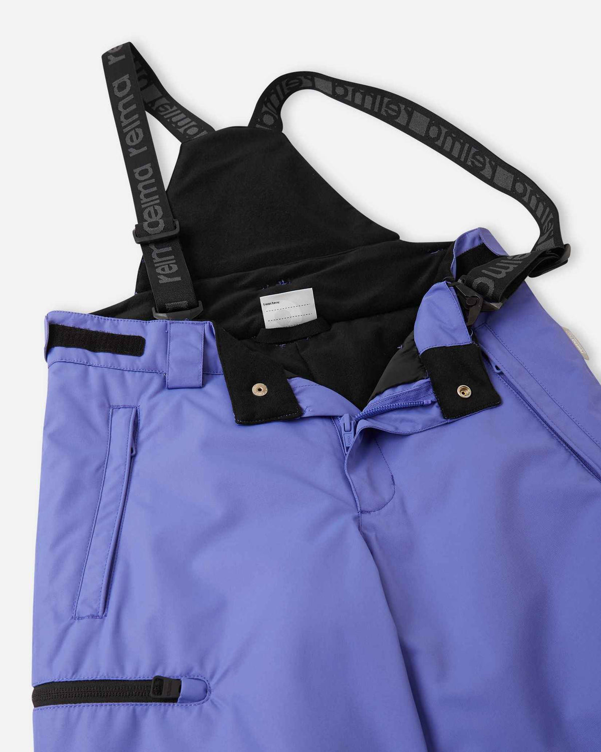 Close-up detail of the front waist on the breezy violet Reima Terrie kids' ski pants, showing the secure snap buttons, smooth zipper fly, soft inner lining, and the front attachment points for the adjustable suspenders.