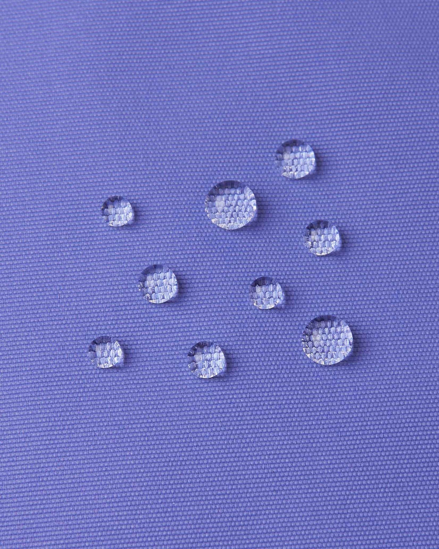 Macro close-up of water droplets actively beading and rolling off the breezy violet outer shell of the Reima Terrie kids' ski pants, visually highlighting the high-performance breathable and waterproof Reimatec technology.