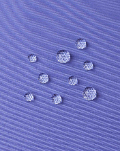 Macro close-up of water droplets actively beading and rolling off the breezy violet outer shell of the Reima Terrie kids' ski pants, visually highlighting the high-performance breathable and waterproof Reimatec technology.