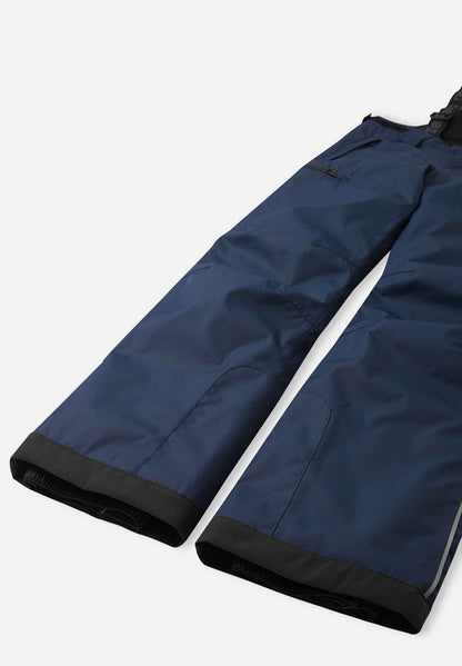 Detail view of the lower legs on the navy blue Reima Terrie kids' ski pants, emphasizing the rugged black reinforced hems to protect against ski edges and the inner elastic snow locks designed to securely grip winter boots.