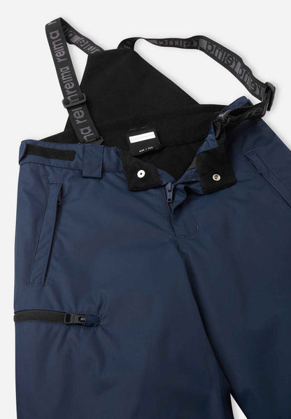 Close-up detail of the front waist on the navy blue Reima Terrie kids' ski pants, showing the secure snap buttons, smooth zipper fly, soft inner lining, and the front attachment points for the adjustable suspenders.