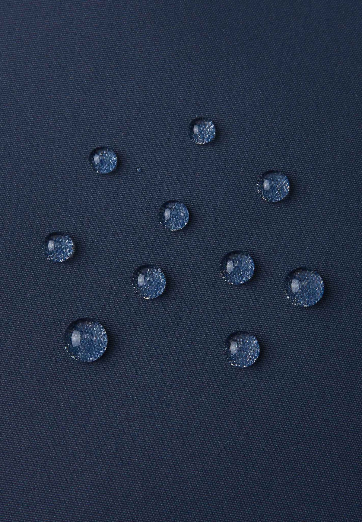 Macro close-up of water droplets actively beading and rolling off the navy blue outer shell of the Reima Terrie kids' ski pants, visually highlighting the high-performance breathable and waterproof Reimatec technology.