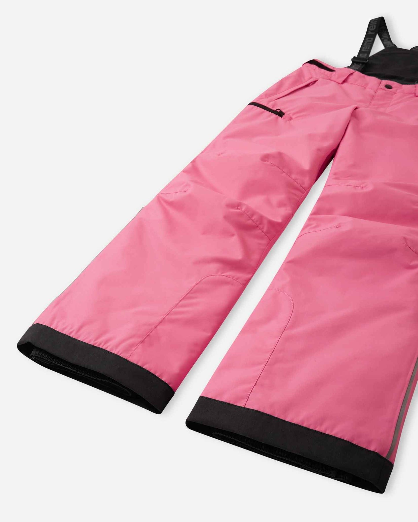 Detail view of the lower legs on the soft coral Reima Terrie kids' ski pants, emphasizing the rugged reinforced hems to protect against ski edges and the inner elastic snow locks designed to securely grip winter boots.