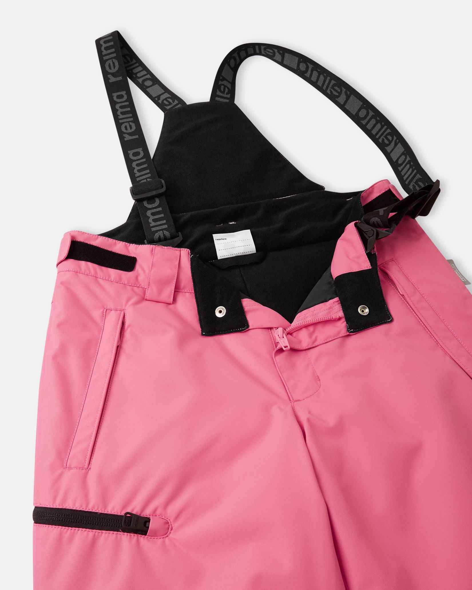 Close-up detail of the front waist on the soft coral Reima Terrie kids' ski pants, showing the secure snap buttons, smooth zipper fly, soft inner lining, and the front attachment points for the adjustable suspenders.