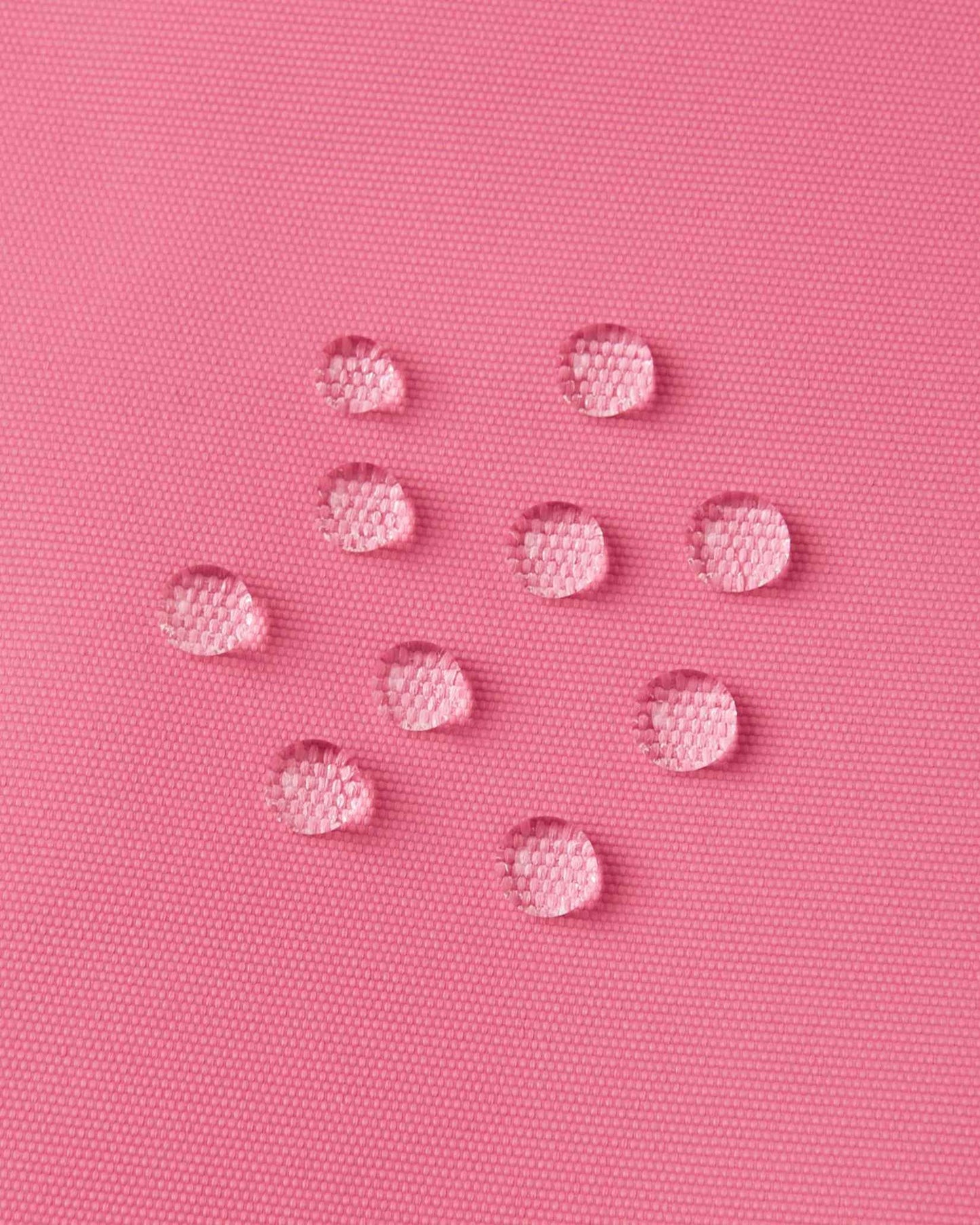 Macro close-up of water droplets actively beading and rolling off the soft coral outer shell of the Reima Terrie kids' ski pants, visually highlighting the high-performance breathable and waterproof Reimatec technology.