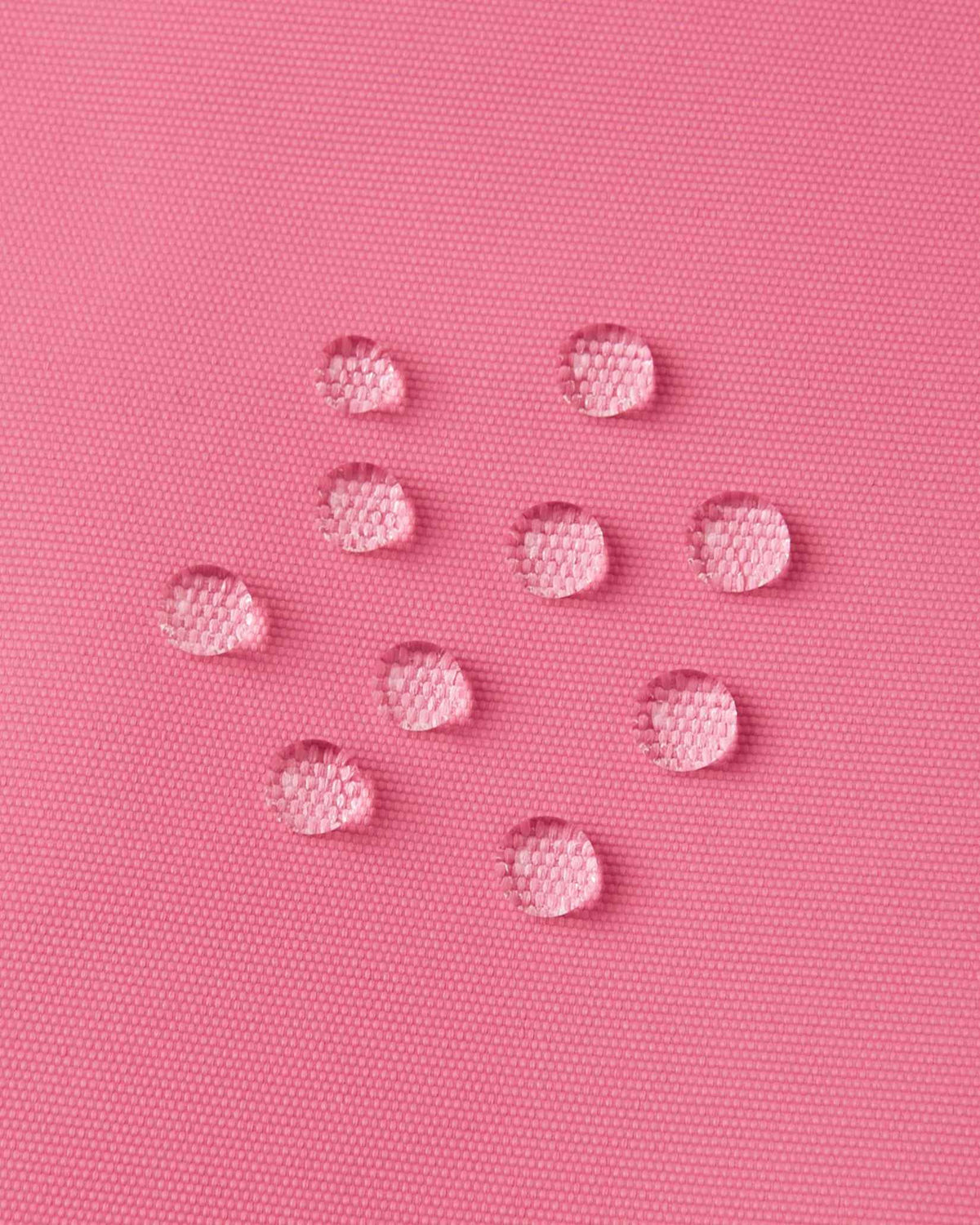 Macro close-up of water droplets actively beading and rolling off the soft coral outer shell of the Reima Terrie kids' ski pants, visually highlighting the high-performance breathable and waterproof Reimatec technology.