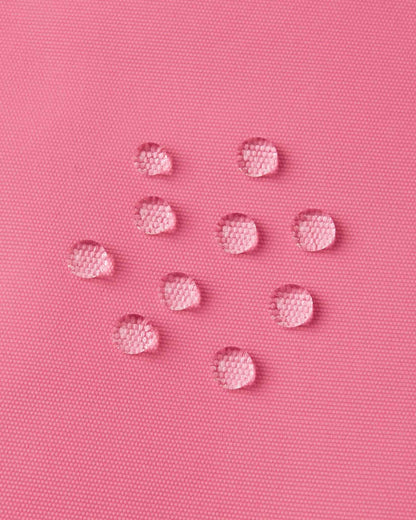 Macro close-up of water droplets actively beading and rolling off the soft coral outer shell of the Reima Terrie kids' ski pants, visually highlighting the high-performance breathable and waterproof Reimatec technology.