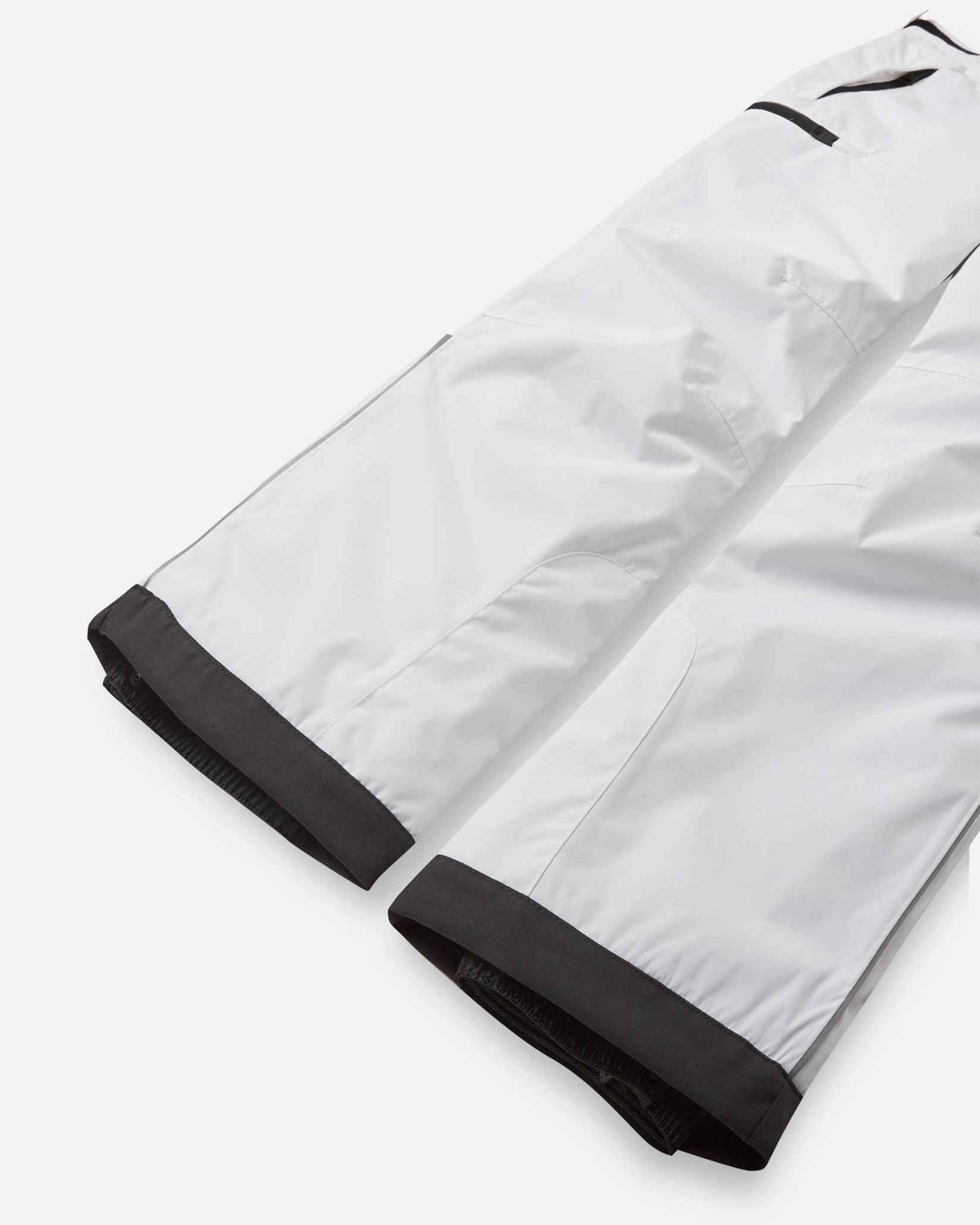 Detail view of the lower legs on the pristine white Reima Terrie kids' ski pants, emphasizing the rugged black reinforced hems designed to protect against sharp ski edges.