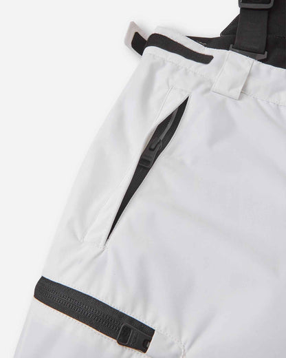 Close-up detail of the hip and thigh on the white Reima Terrie kids' ski pants, highlighting secure black zippered pockets and adjustable hook-and-loop waist tabs for a custom, draft-free fit.