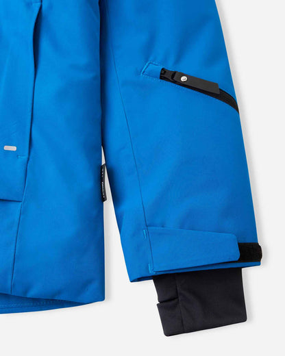 Close-up of the left forearm on the bright blue Reima Tieten boys' snow jacket, featuring a black zippered lift pass pocket, adjustable wrist strap, and an inner thumbhole lycra cuff to seal out snow.