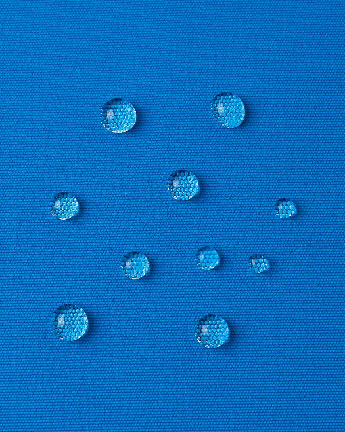 Extreme close-up of distinct water droplets resting on the bright blue textile of the Reima Tieten jacket, highlighting the high-performance, dirt- and water-repellent BIONIC-FINISH ECO treatment.