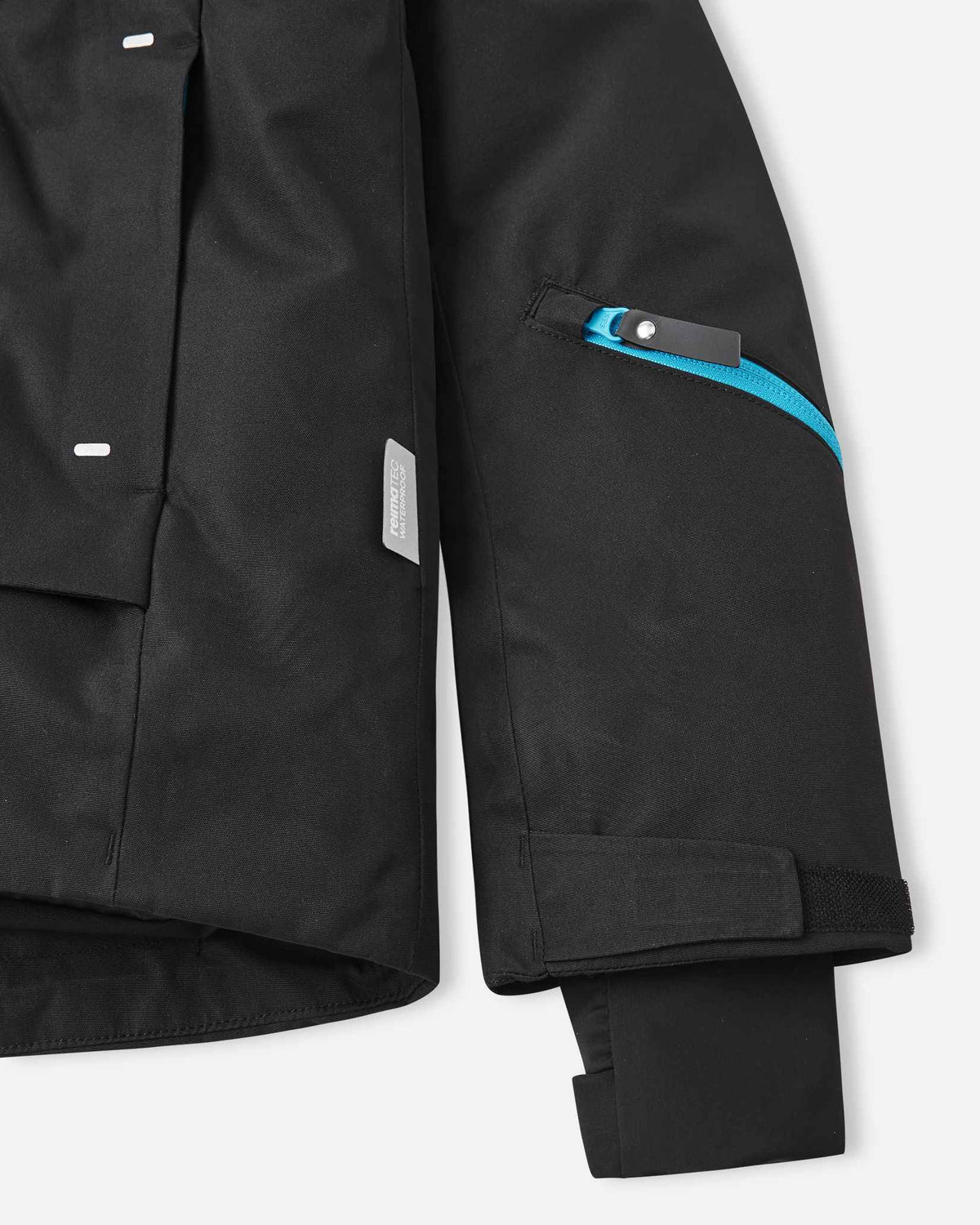 Close-up of the left forearm and cuff on the black Reima Tieten children's snowboard coat, highlighting the Reimatec waterproof tag, adjustable wrist strap, and inner lycra thumbhole gaiter.