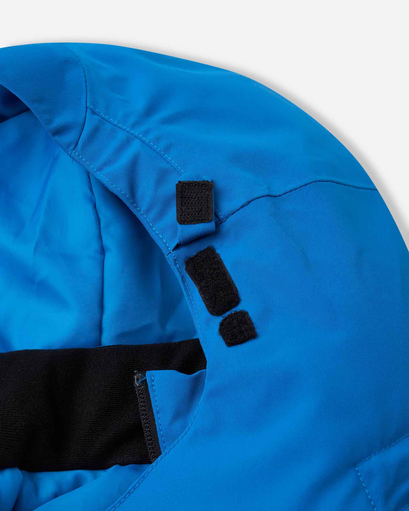 Detail shot of the collar edge on the bright blue Reima Tieten kids' ski coat, revealing the reinforced hook-and-loop tabs that securely anchor the removable hood in place during active use.