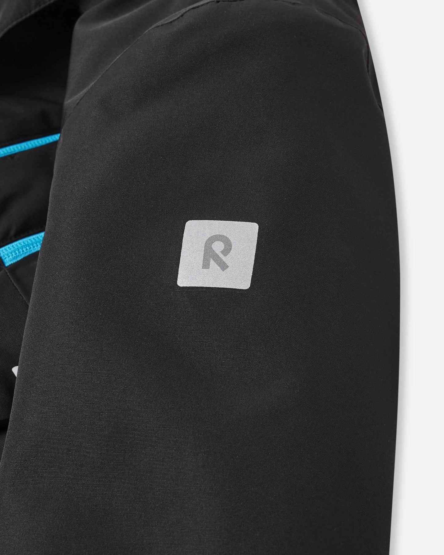 The reflective Reima brand logo sits on the upper arm of the black Tieten kids ski jacket for better visibility.