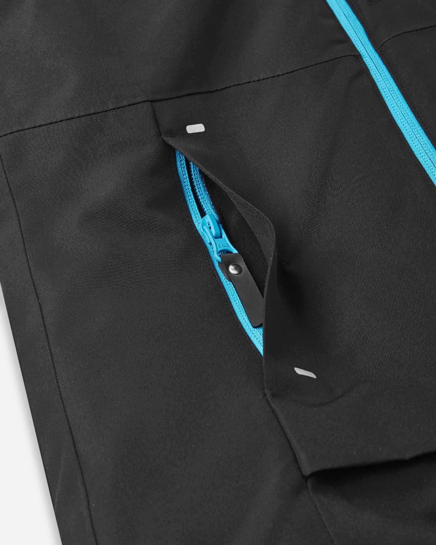 A bright blue zipper on the left sleeve of the black Reima jacket opens a small pocket designed for holding ski passes.