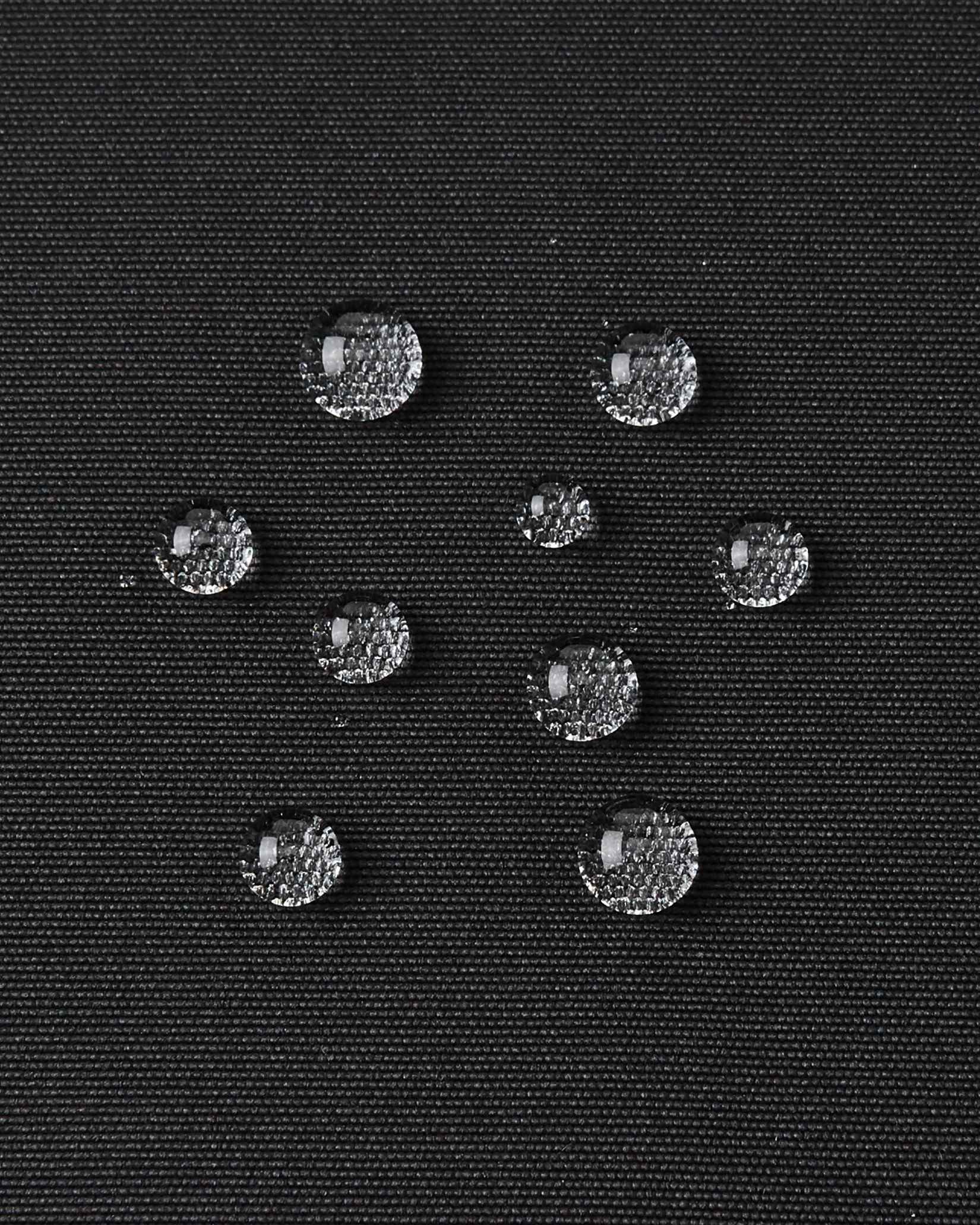 Water droplets bead up on the black outer material of the kids Reima Tieten ski jacket to show its waterproof finish.