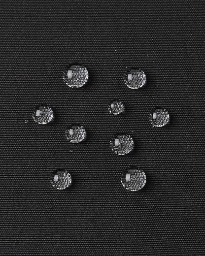 Water droplets bead up on the black outer material of the kids Reima Tieten ski jacket to show its waterproof finish.