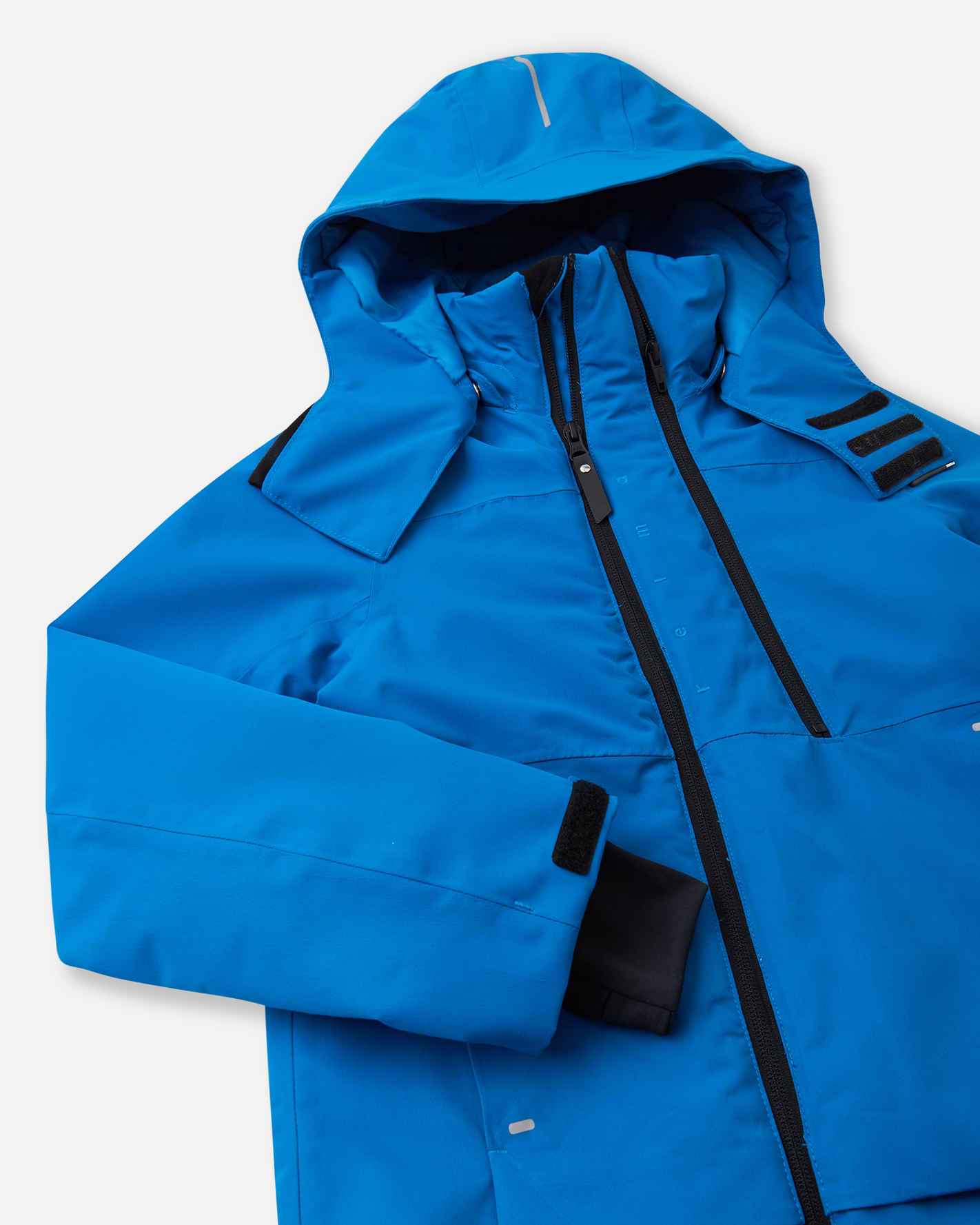 Detailed close-up of the chest on the bright blue Reima Tieten kids' waterproof jacket, highlighting the dual black zippers used for core ventilation and a high wind-blocking chin guard.