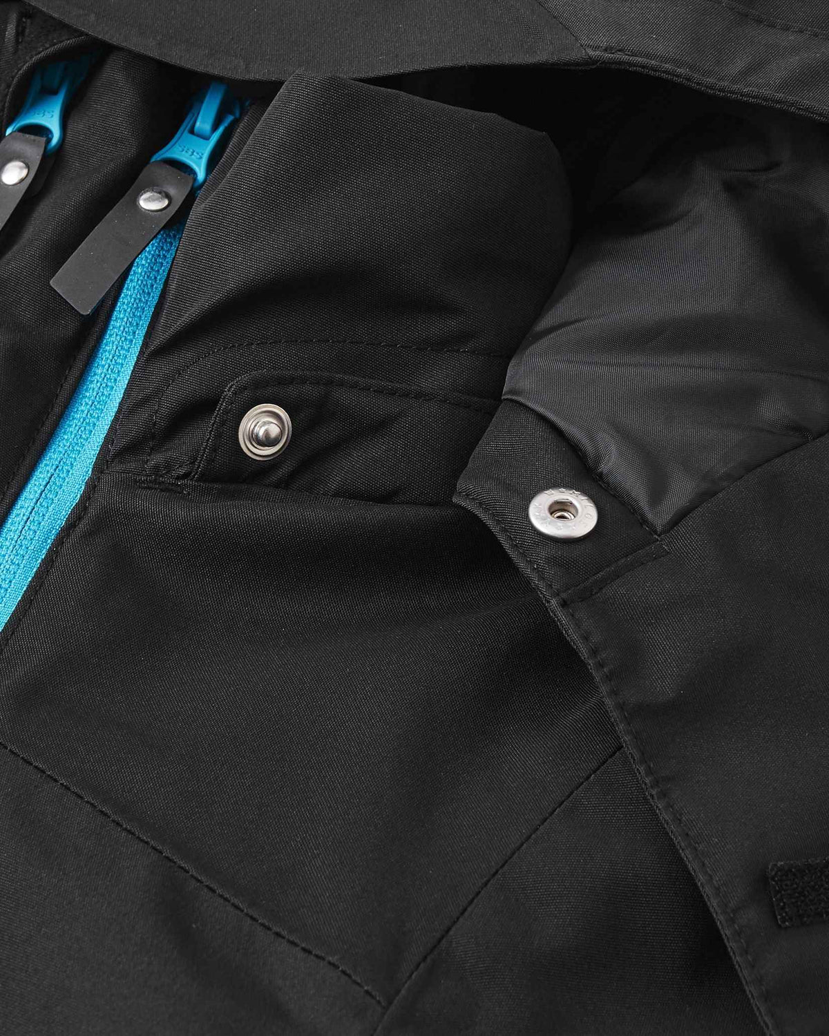 Detailed shot of the neckline on the black Reima Tieten kids' winter sports jacket, showing the top of the cyan zipper gusset and the tear-away metallic snaps for the removable safety hood.