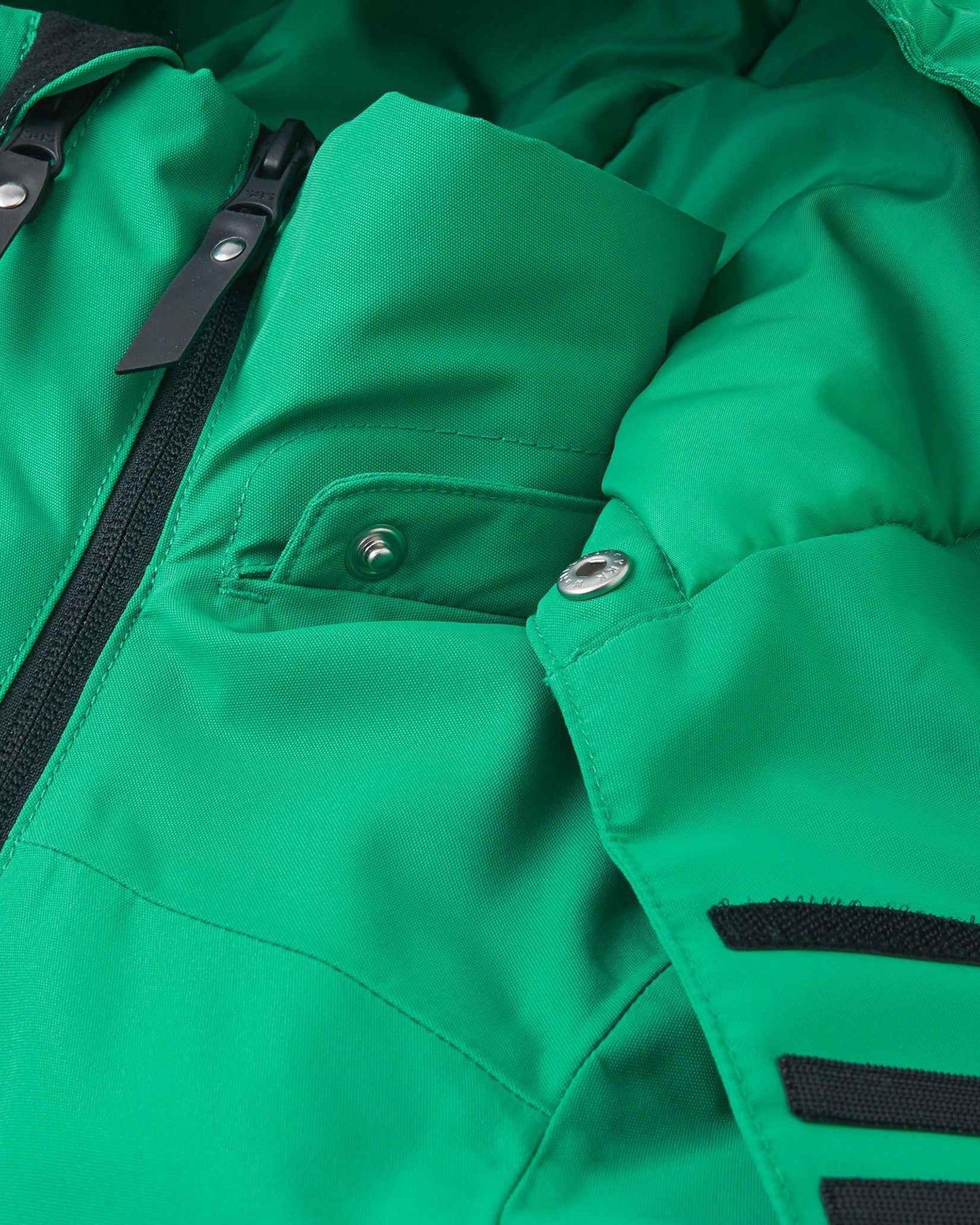 A close view of the green Reima Tieten kids ski jacket shows the front zipper securely closed near the neck to block cold wind.