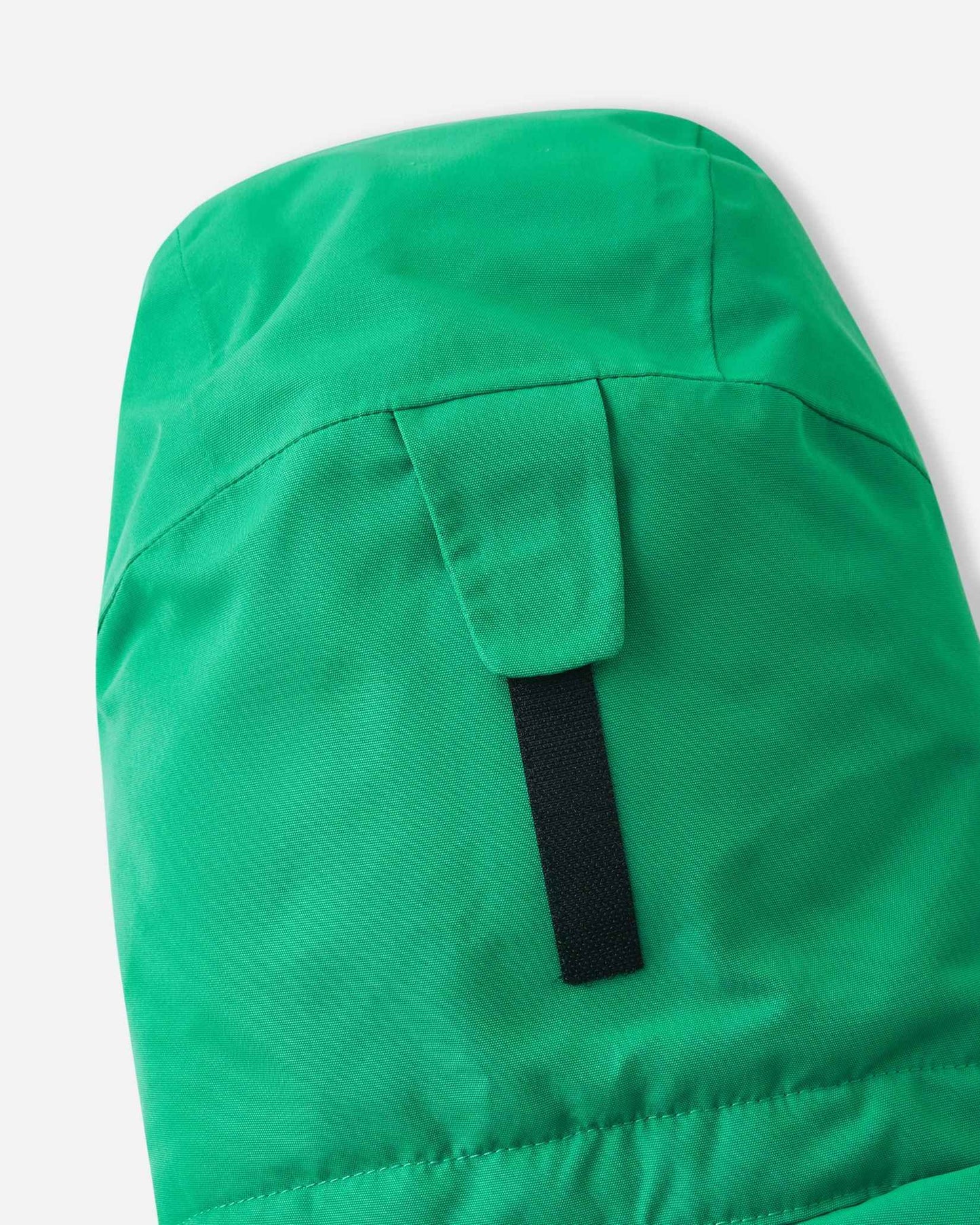 A black velcro strap sits on the back of the green Reima ski jacket hood for easy size adjustments.
