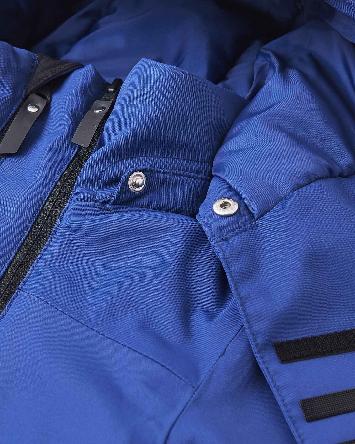 The top collar of the blue winter jacket sits open to reveal metal snap buttons and a dark interior lining.