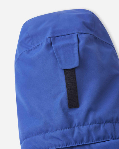 A black velcro strap sits on the back of the blue Reima ski jacket hood for quick size adjustments.