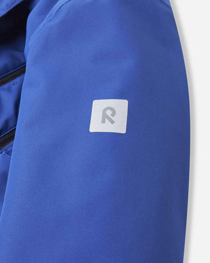 A square reflective Reima logo patch rests on the upper sleeve of the bright blue ski coat.