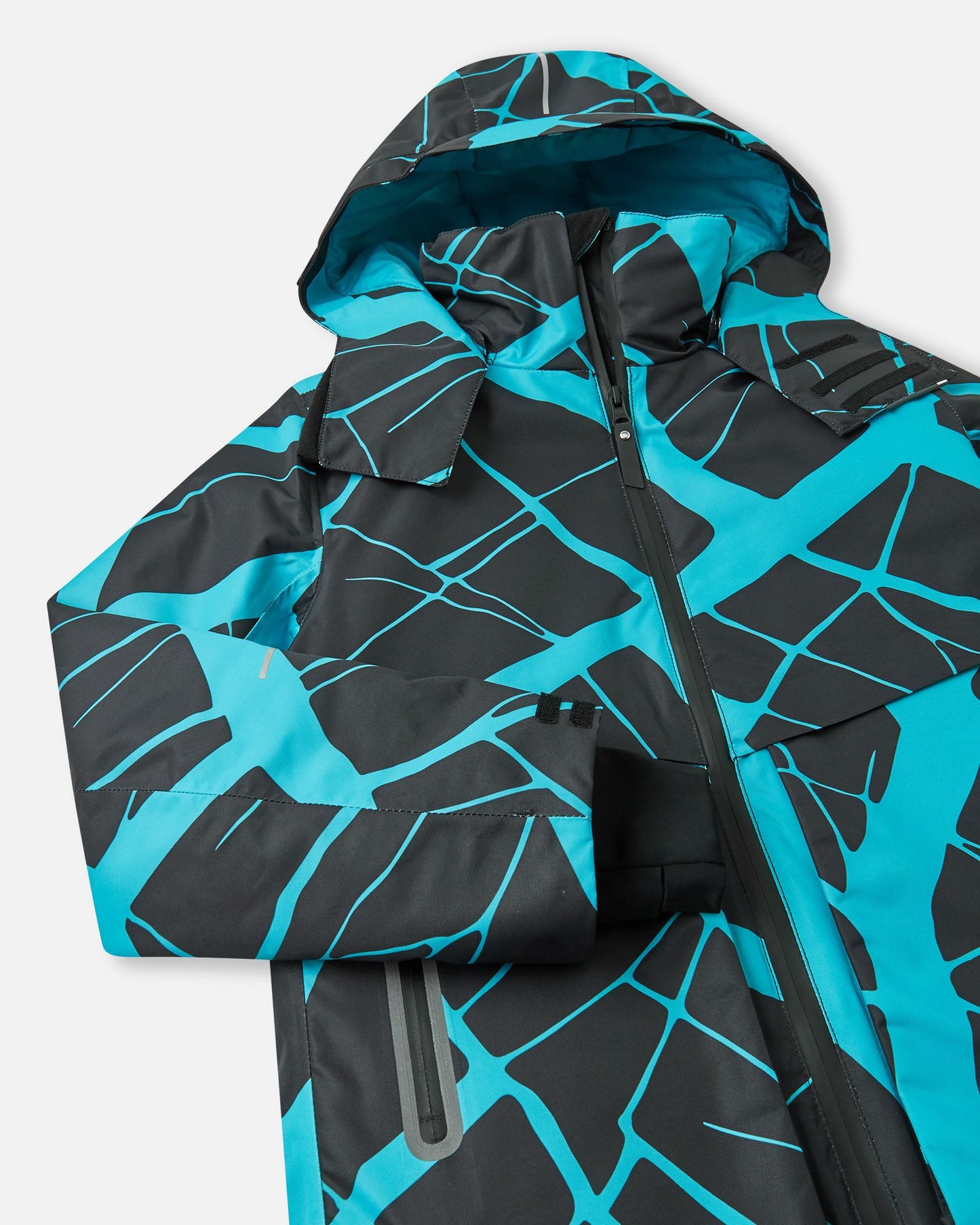 Close-up detail of the black Reima Tirro kids' waterproof ski jacket, highlighting the durable sealed main zipper, high protective collar, and dynamic blue geometric design.