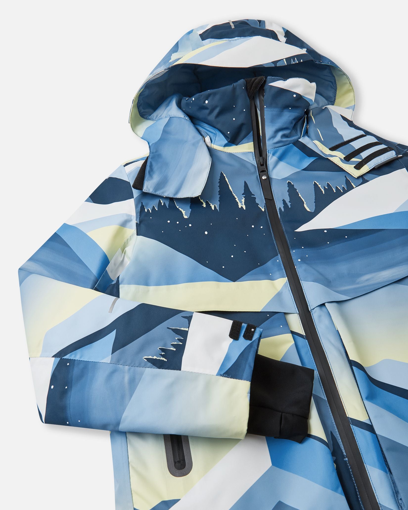Close-up detail of the ocean blue Reima Tirro kids' waterproof ski jacket, highlighting the durable sealed main zipper, protective storm flap, and dynamic mountain graphic design.